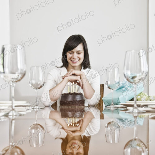 Mature woman seated at a table set for dinner looking at a large chocolate birthday cake Mature woman seated at a table set for dinner looking at a large chocolate birthday cake