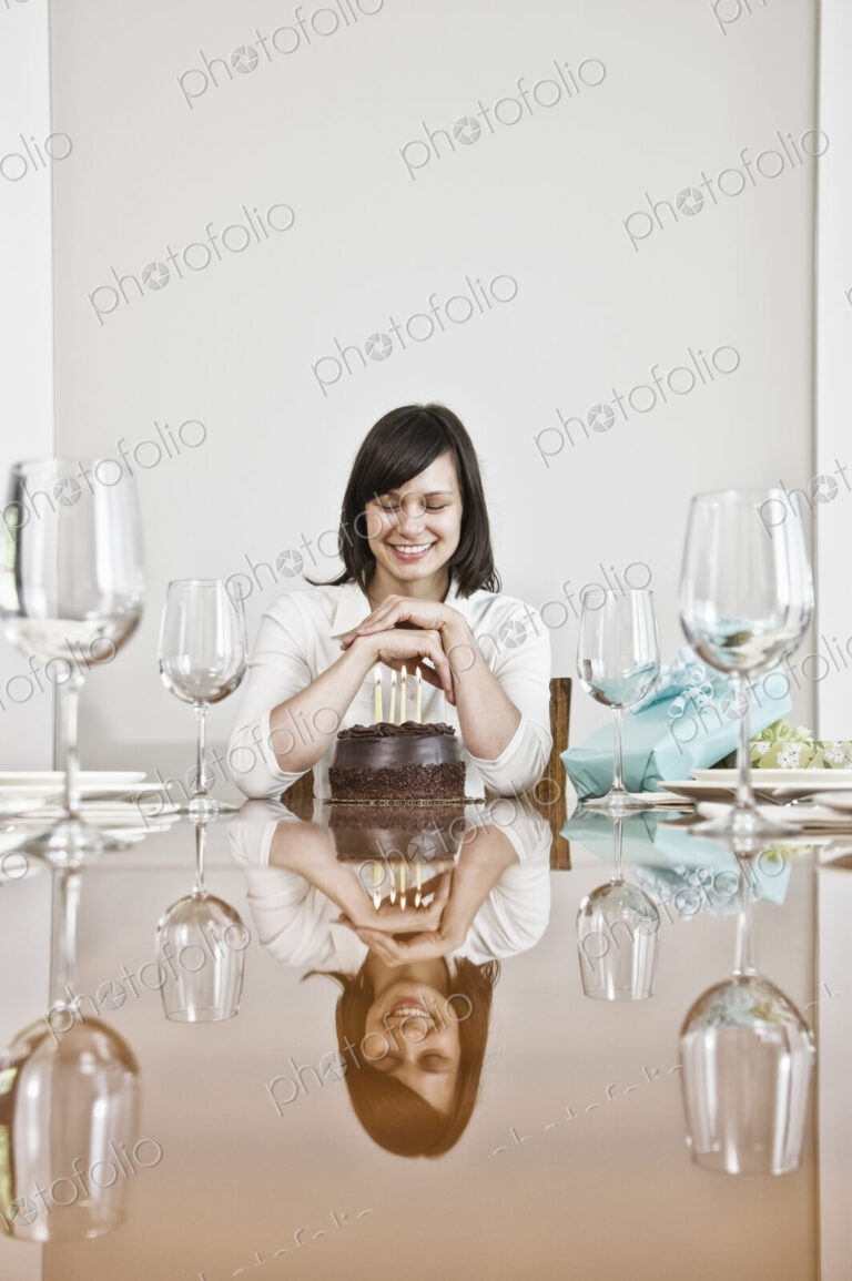Mature woman seated at a table set for dinner looking at a large chocolate birthday cake