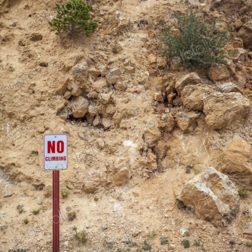 Metal "No Climbing" sign with red lettering on a post, placed at the base of a rugged… Metal "No Climbing" sign with red lettering on a post, placed at the base of a rugged…
