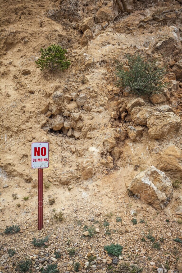 Metal "No Climbing" sign with red lettering on a post, placed at the base of a rugged…