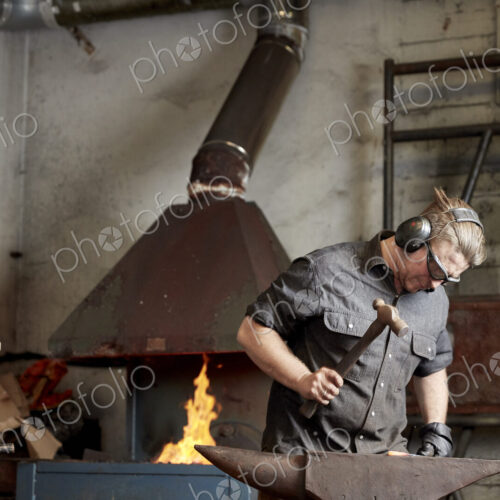 Metal worker using a hammer to shape a red hot piece of metal on an anvil. Metal worker using a hammer to shape a red hot piece of metal on an anvil.