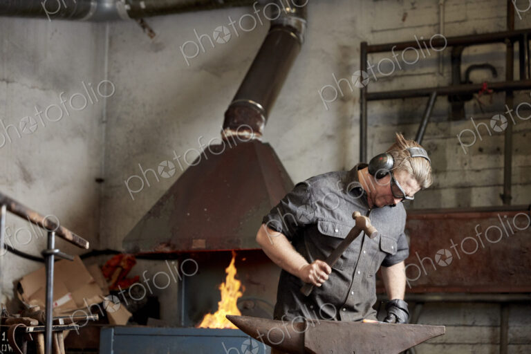Metal worker using a hammer to shape a red hot piece of metal on an anvil.