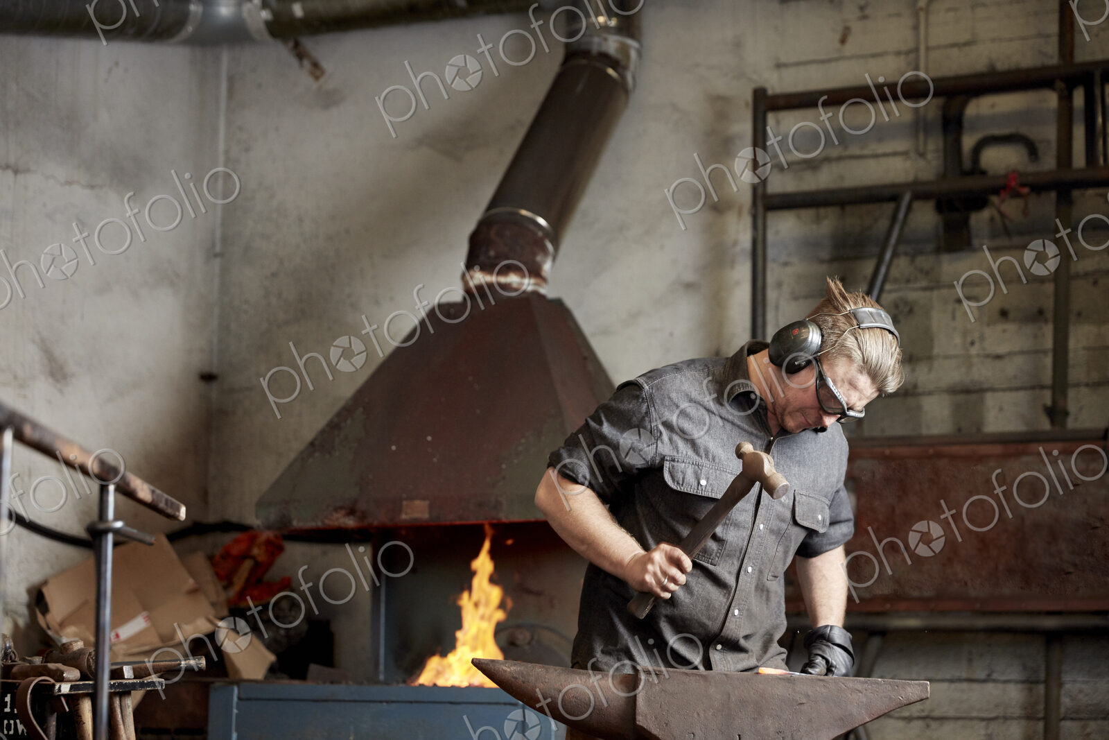 Metal worker using a hammer to shape a red hot piece of metal on an anvil.