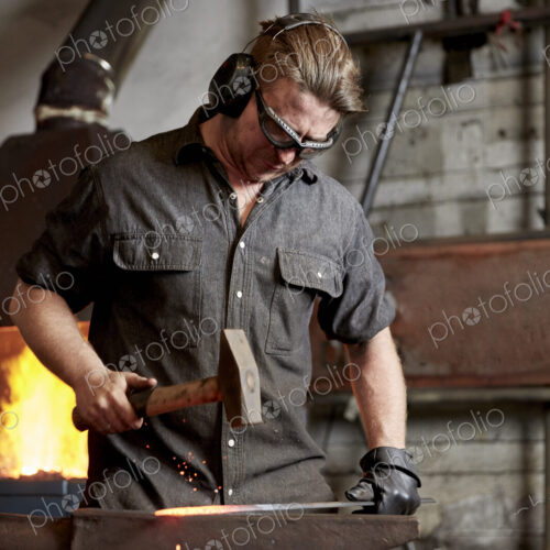 Metal worker using a hammer to shape a red hot piece of metal on an anvil. Metal worker using a hammer to shape a red hot piece of metal on an anvil.