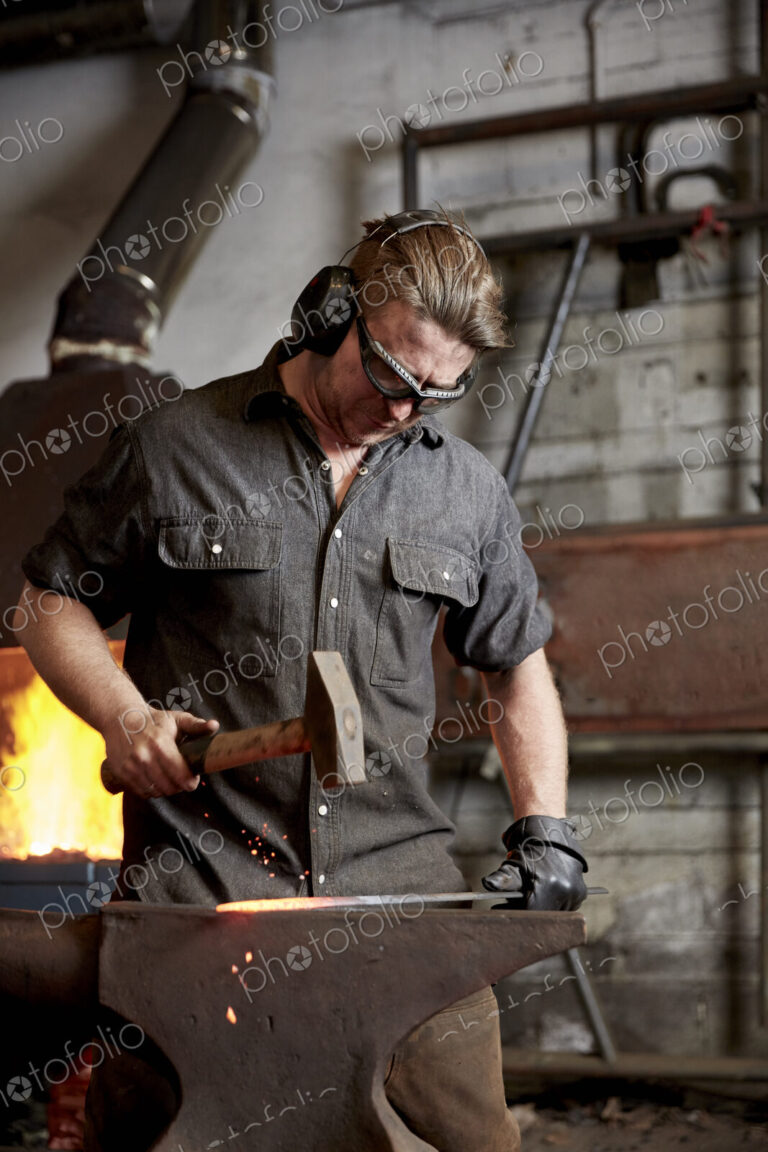 Metal worker using a hammer to shape a red hot piece of metal on an anvil.