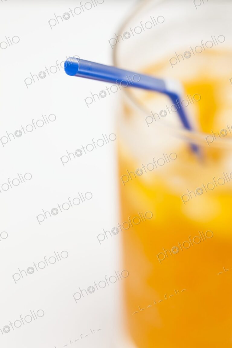 Minimalist close-up of a blue straw in a cold orange beverage with ice. Bright,…