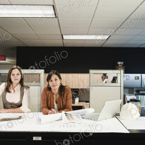 Mixed race and Caucasian females working on a project at a table in their office. Mixed race and Caucasian females working on a project at a table in their office.