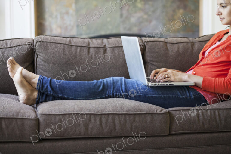 Mixed race caucasian woman at home on the couch working on a lap top computer with her…