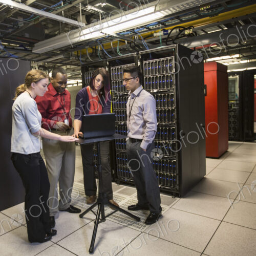 Mixed race group of technicians doing diagnostic tests on servers in a large server farm.