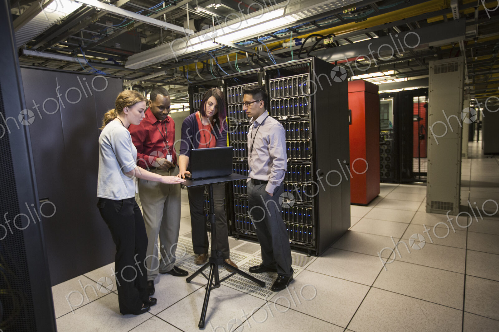 Mixed race group of technicians doing diagnostic tests on servers in a large server farm.