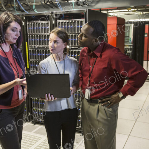 Mixed race group of technicians doing diagnostic tests on servers in a large server farm.