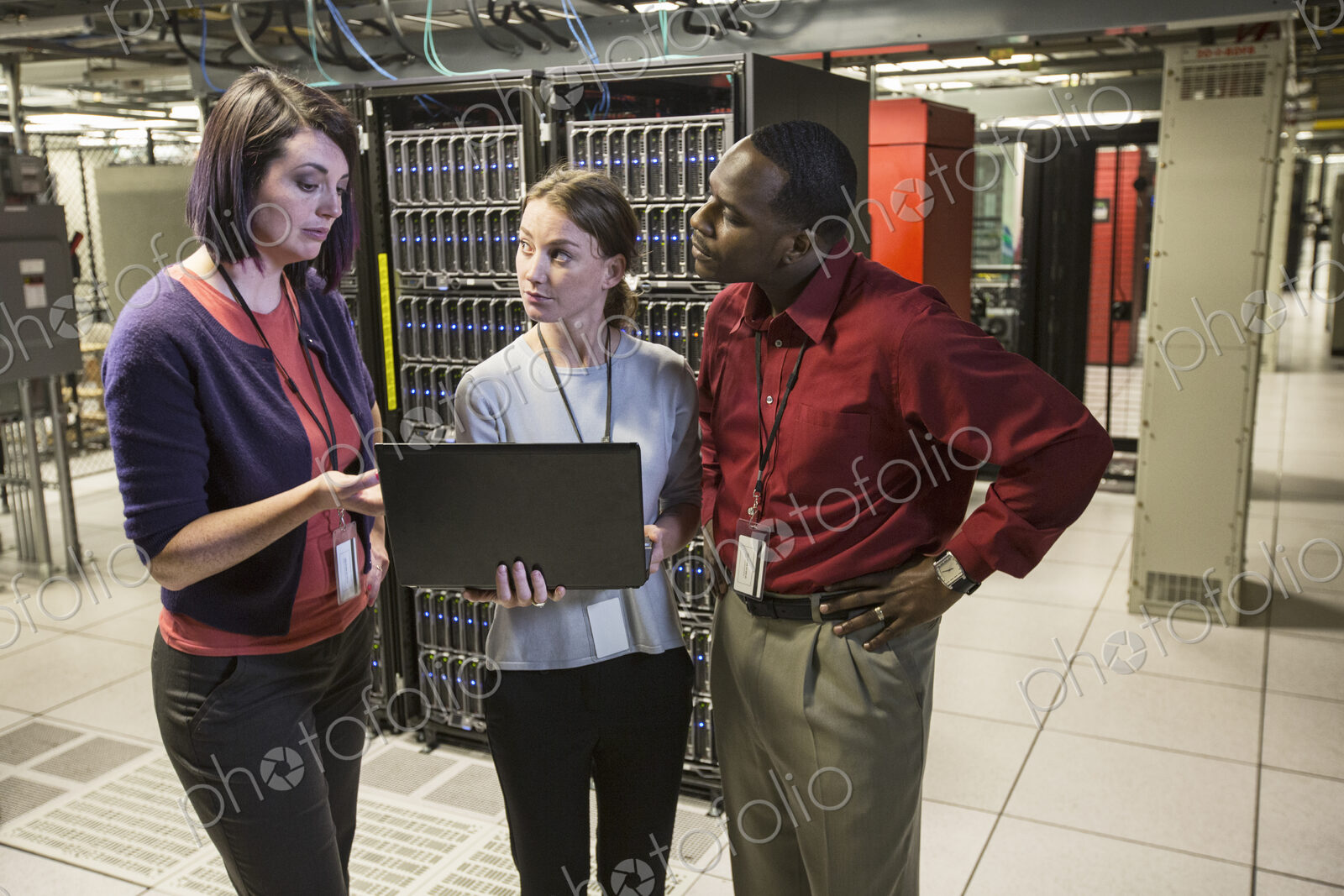 Mixed race group of technicians doing diagnostic tests on servers in a large server farm.