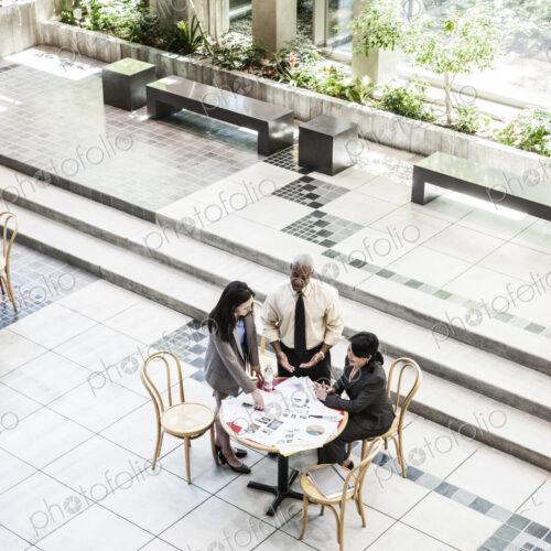 Mixed race group of three people in an informal meeting around a table in a lobby area. Mixed race group of three people in an informal meeting around a table in a lobby area.