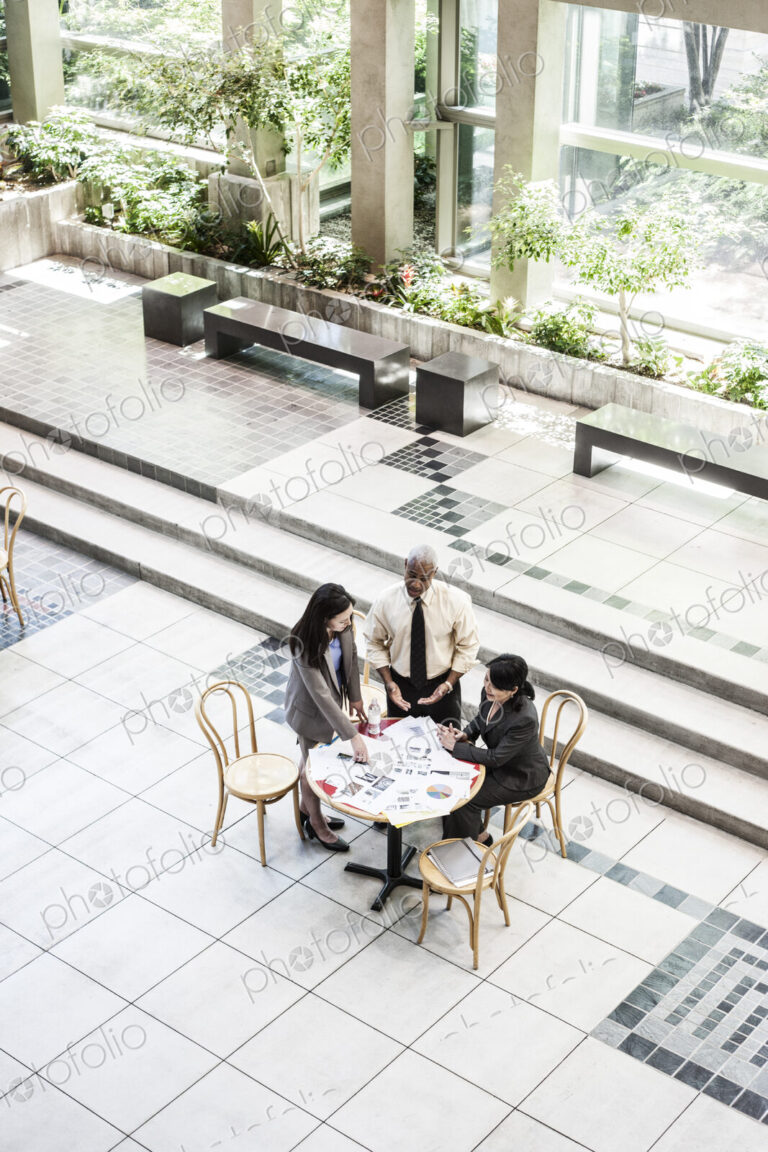Mixed race group of three people in an informal meeting around a table in a lobby area.