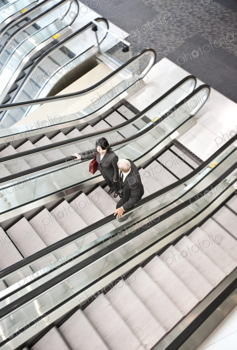 Mixed race pair of business people on the way to a meeting near a set of escalators.