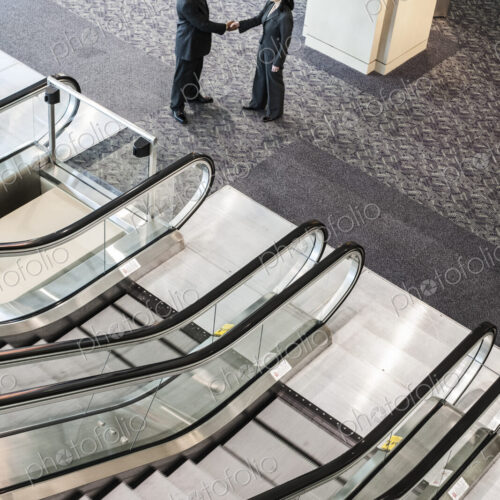 Mixed race pair of business people on the way to a meeting near a set of escalators. Mixed race pair of business people on the way to a meeting near a set of escalators.
