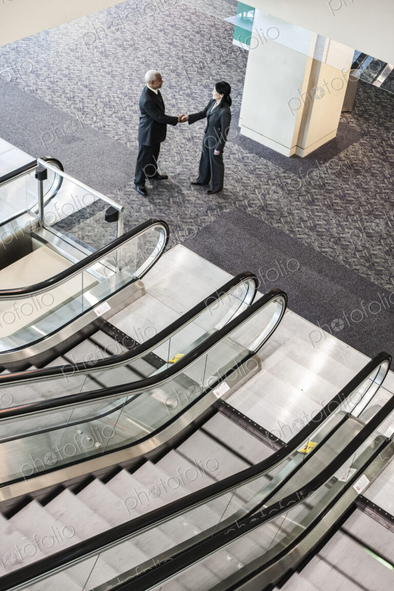 Mixed race pair of business people on the way to a meeting near a set of escalators.