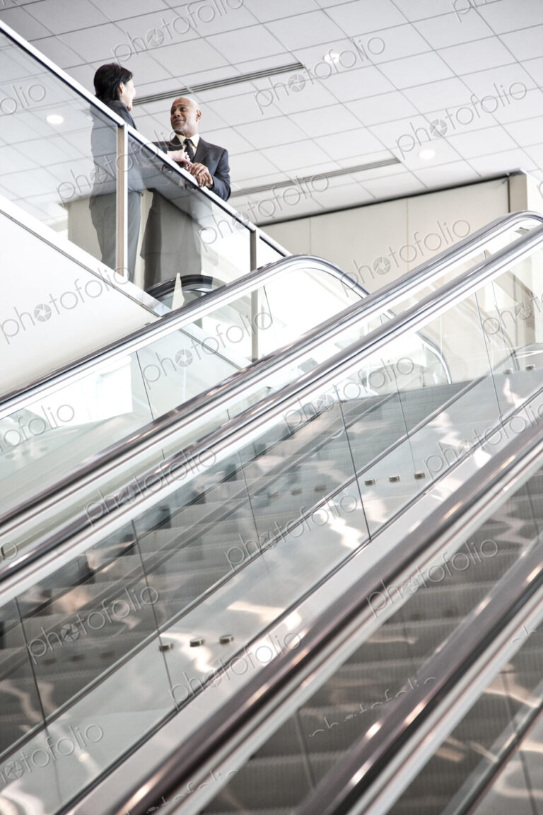 Mixed race pair of business people on the way to a meeting near a set of escalators.