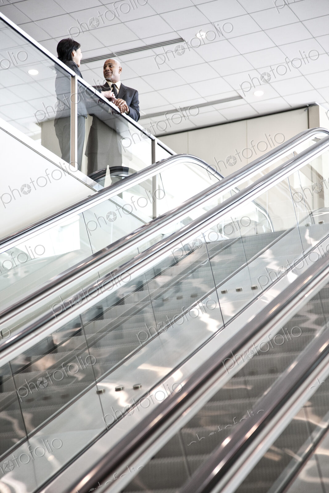 Mixed race pair of business people on the way to a meeting near a set of escalators.