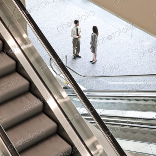 Mixed race pair of business people on the way to a meeting near a set of escalators. Mixed race pair of business people on the way to a meeting near a set of escalators.