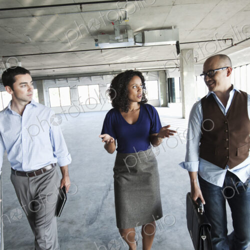 Mixed race team of business people touring a new empty raw office space.