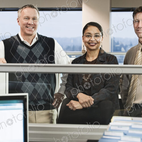 Mixed race team of three business people in their cubicle style office.