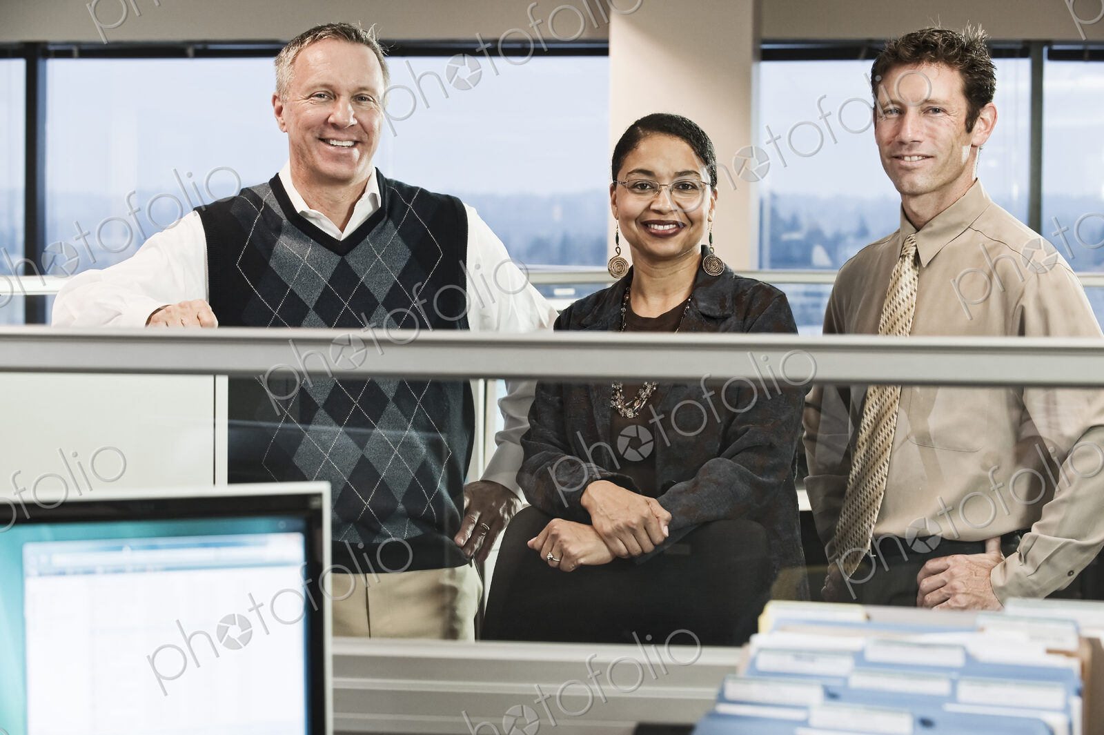 Mixed race team of three business people in their cubicle style office.
