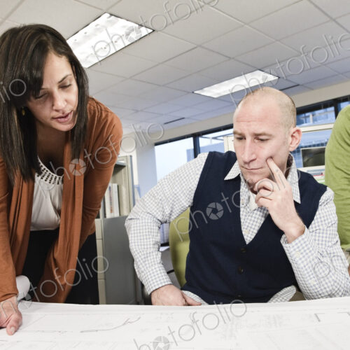 Mixed race team of three people working on a project in a cubicle office.