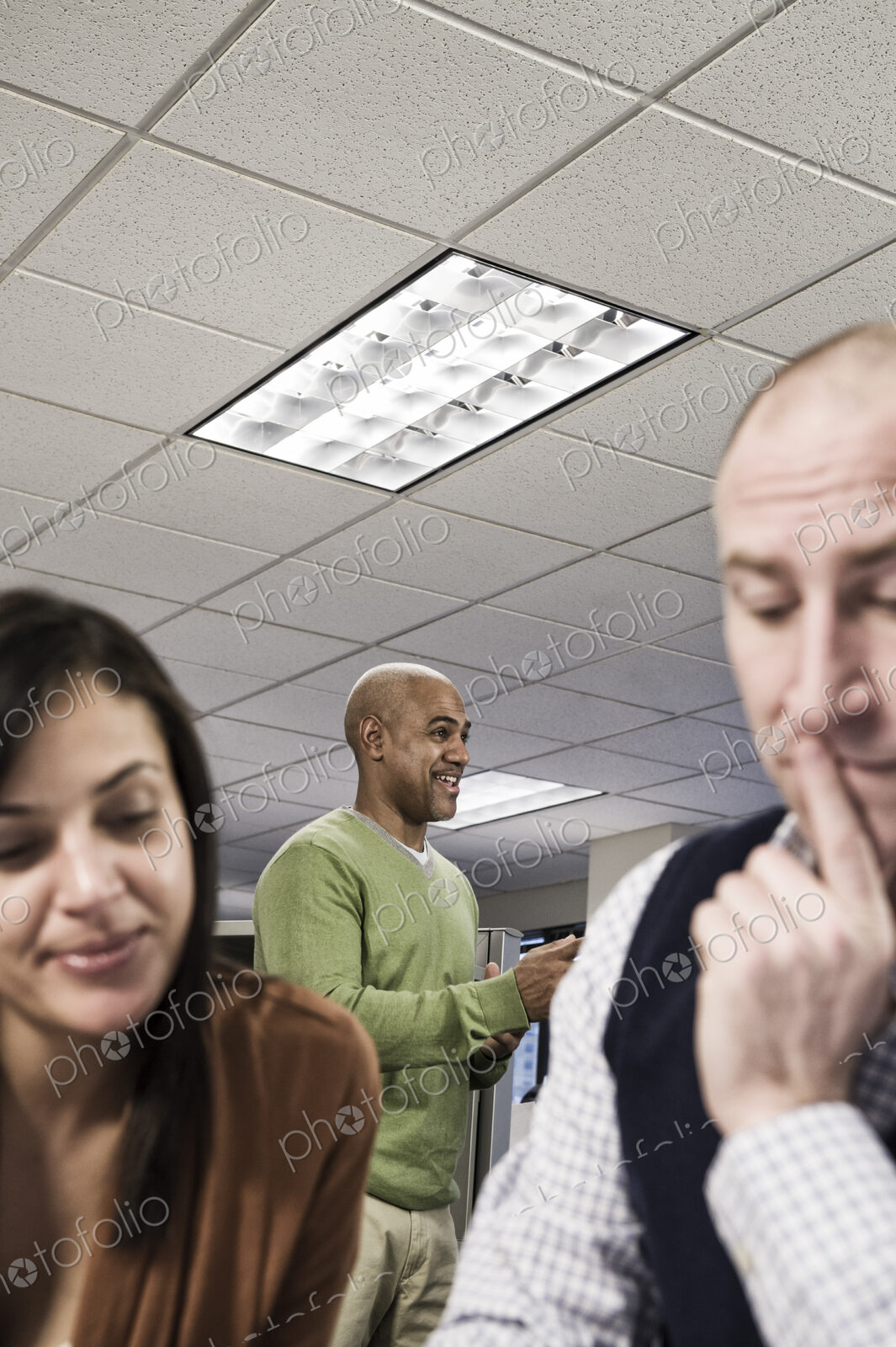 Mixed race team of three people working on a project in an office cubicle area.