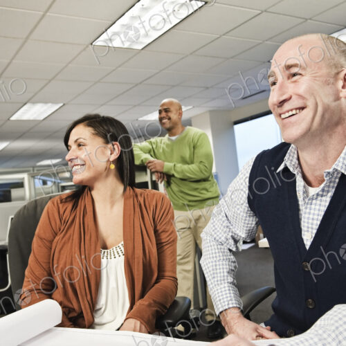 Mixed race team of three people working on a project in an office cubicle area. Mixed race team of three people working on a project in an office cubicle area.