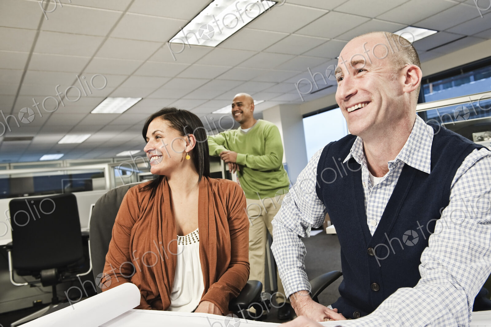 Mixed race team of three people working on a project in an office cubicle area.