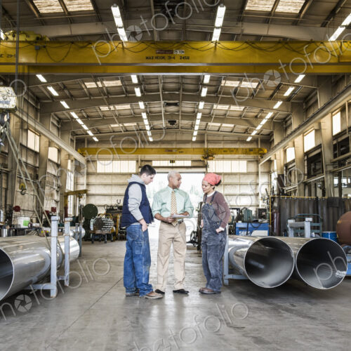 Mixed race team of workers and management people in a large sheet metal factory