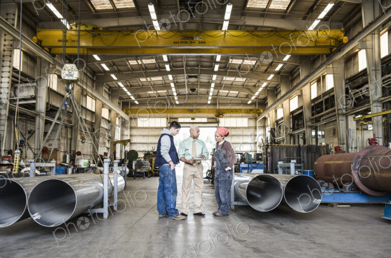 Mixed race team of workers and management people in a large sheet metal factory