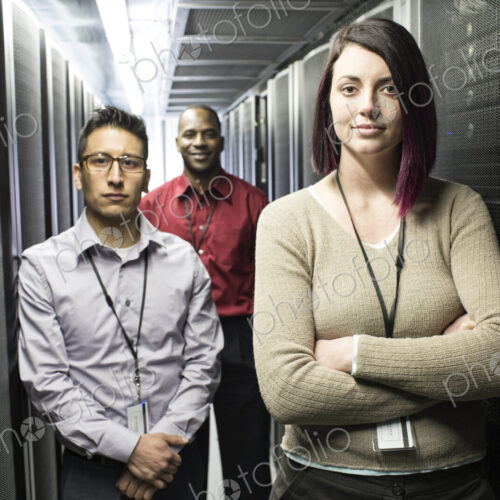 Mixed race technical team in an aisle of a large computer server farm.