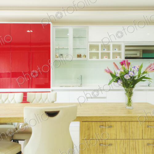 Modern kitchen with red cabinets, two sinks, gas stove, fitted cupboards with red…