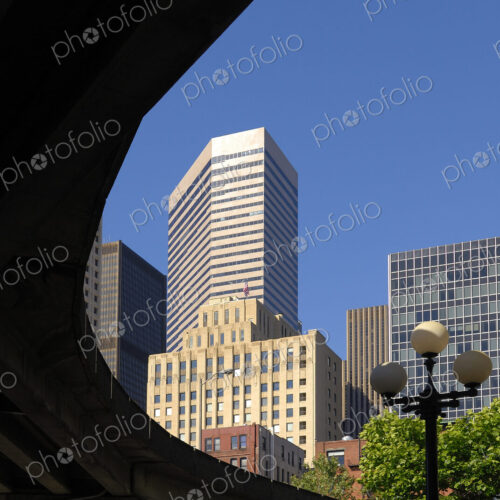 Modern skyscraper behind an elevated road or railway with streetlight in park below.