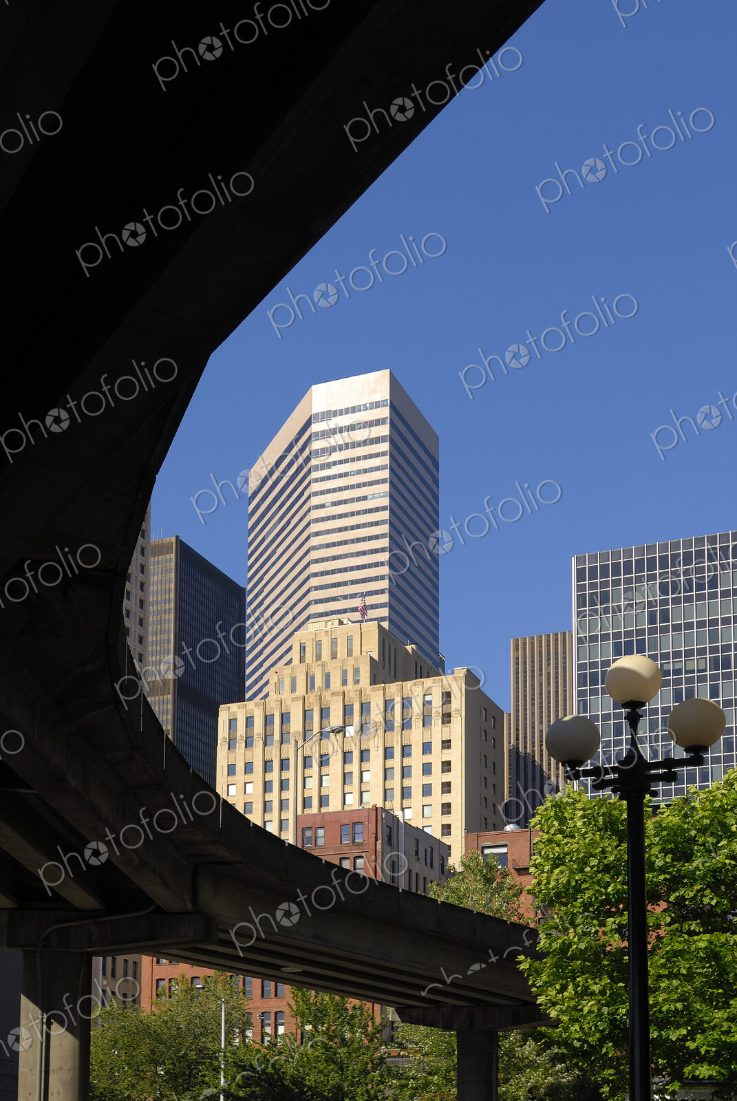 Modern skyscraper behind an elevated road or railway with streetlight in park below.