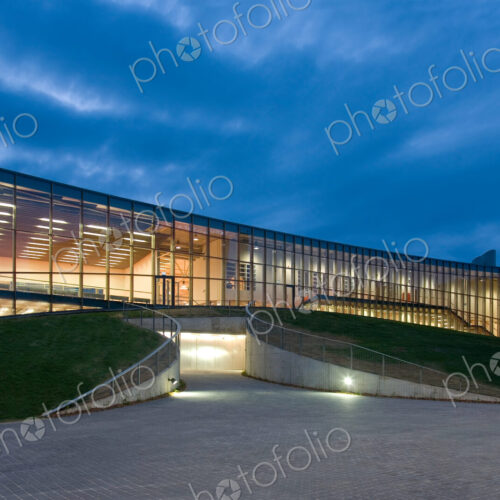 Modern university buildings, glass facade lit up at night, on a curved ground surface