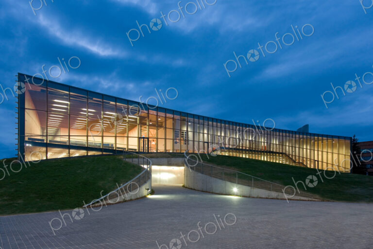 Modern university buildings, glass facade lit up at night, on a curved ground surface