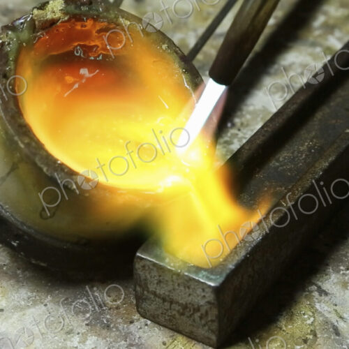 Molten metal, gold being poured into a mould for setting.