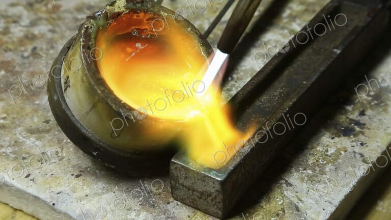 Molten metal, gold being poured into a mould for setting.