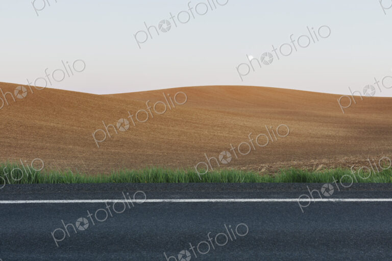 Moonrise over rolling freshly planted fields, road in foreground