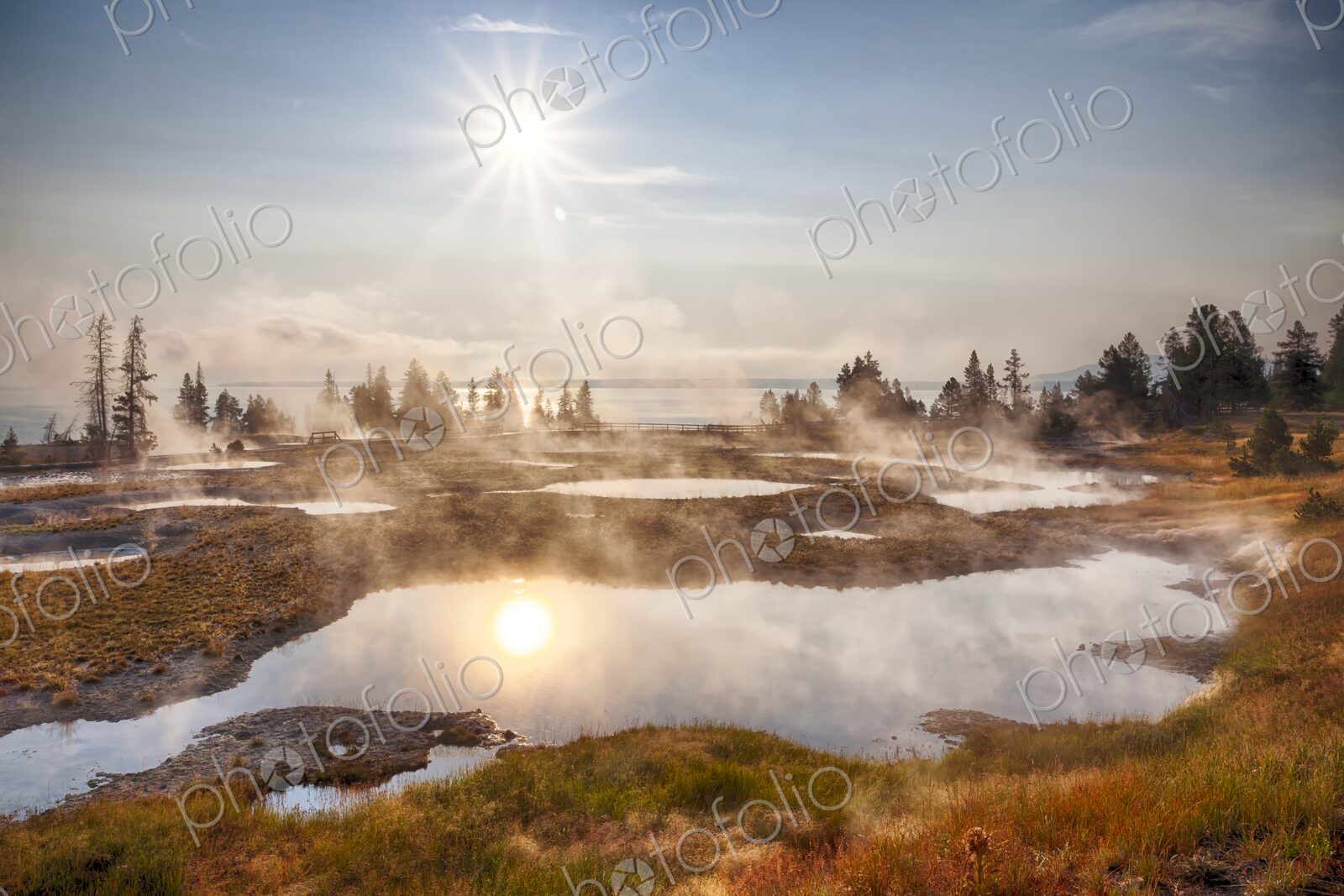 Morning sun glows over steaming geyser pools in Yellowstone’s West Thumb Geyser Basin,…