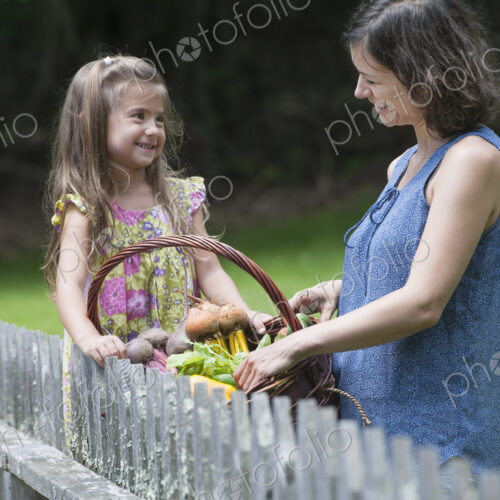 Mother and daughter standing in a garden with a basket of vegetables. Mother and daughter standing in a garden with a basket of vegetables.