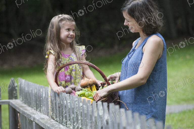 Mother and daughter standing in a garden with a basket of vegetables.