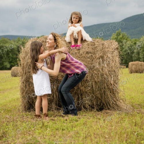 Mother playing outdoors with her daughters lifting them on top of a haystack. Mother playing outdoors with her daughters lifting them on top of a haystack.
