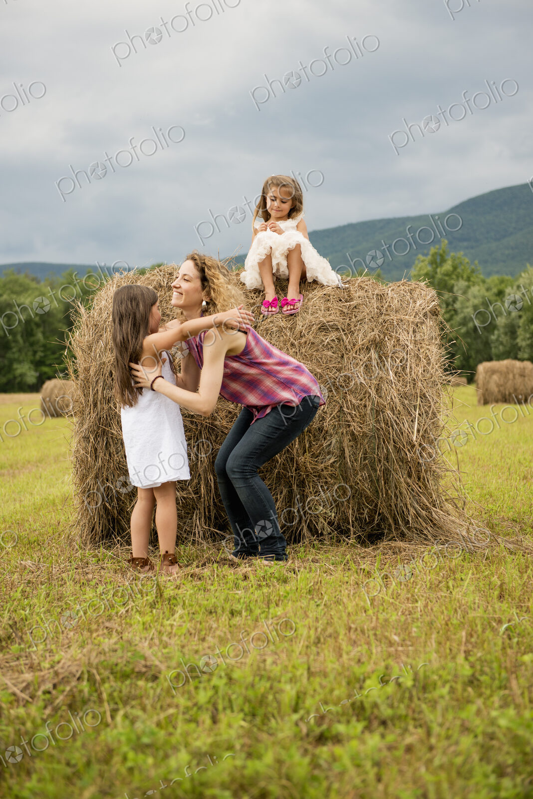 Mother playing outdoors with her daughters lifting them on top of a haystack.