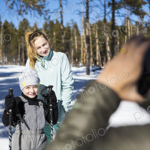 Mother taking a picture of her two children, a boy and teenage girl in snowy forest…