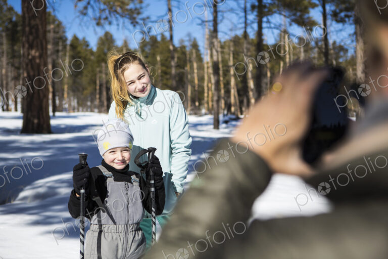 Mother taking a picture of her two children, a boy and teenage girl in snowy forest…