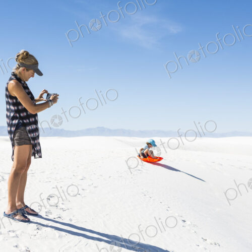Mother taking picture of son sledding on sand dunes Mother taking picture of son sledding on sand dunes